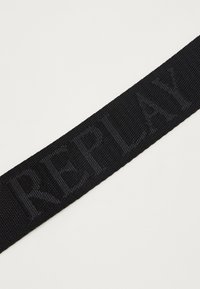 Sort vævet bælte med hævet "REPLAY" tekst. Strukturen har en glat finish, der fremhæver mærket tydeligt.