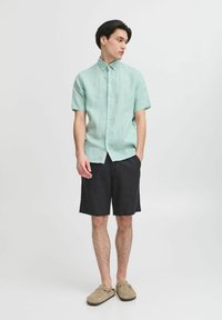 Rövidujjú, menta zöld gombos ing, len anyagból, sötét rövidnadrággal párosítva. Hétköznapi lábbeli, laza fazon, egyszerű design.