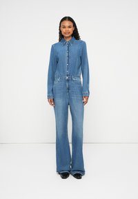 Denim jumpsuit with a collared neckline, front buttons, and wide legs. Features a fitted waist and two side pockets. Light blue color.