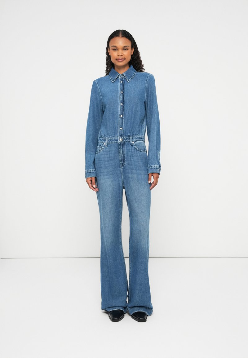 Denim jumpsuit with a collared neckline, front buttons, and wide legs. Features a fitted waist and two side pockets. Light blue color.