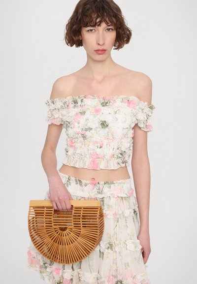 Off-the-shoulder floral top with ruffled edges, paired with a flowy skirt and a round bamboo handbag featuring vertical slats and a wooden handle.