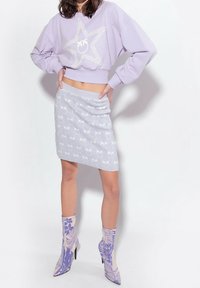 Lilac-värinen lyhyt collegepaita, jossa tähtikuvio, harmaa hyvin istuva hame, jossa on palmulehtikuvio, ja kuvioidut nilkkurit pastellisävyissä.