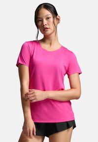 Camiseta deportiva de manga corta en rosa brillante, fabricada con un tejido transpirable, que presenta un escote redondo y una textura sutil. Combinada con pantalones cortos negros.