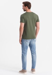 Oliven grøn T-shirt med korte ærmer, blødt stof, rund halsudskæring, parret med lyseblå jeans, afslappet pasform og grå sneakers.