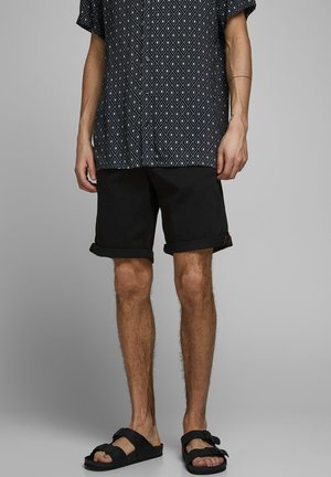 Chemise à manches courtes noire et blanche à motifs, short noir retroussé, et sandales noires. La chemise présente un motif géométrique.