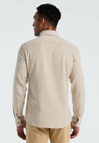 Lichtbeige langemouwen shirt met een kraag, knoopmanchetten en een soepele textuur. Heeft een gebogen zoom en subtiele stikseldetails.