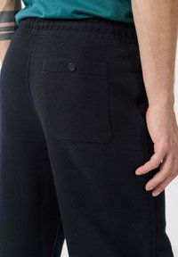 Zwarte joggingbroek met een elastische tailleband, voorzien van een achterzak met knoopsluiting en een zachte, textuurstof.