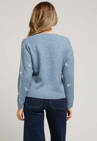 Pull léger bleu à coupe décontractée, arborant des broderies florales sur les manches et un ourlet côtelé, fabriqué en matière tricotée douce.