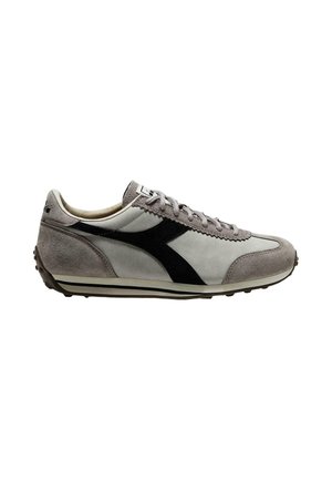 Zapatilla deportiva gris y blanca con franja lateral negra, cordones delanteros y suela texturizada, mostrada de lado sobre un fondo blanco.