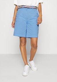 Jasnoniebieskie bawełniane szorty o prostym kroju, z paskiem w paski i bocznymi kieszeniami. Połączone z białymi trampkami.