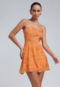Oranje bloemenjurk met geplooide lijf en dunne bandjes. Vloeiende A-lijn rok. Lichtgewicht, gestructureerde stof met een zacht patroon.