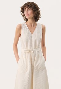 Witte mouwloze jurk met een V-hals, textuurstof met een ruitpatroon, een gecinched taille met een strikceintuur en zijzakken.