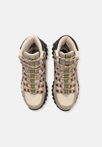 Beige hiking shoes with gray accents, patterned laces in green and red, rugged black sole, and padded ankle support.