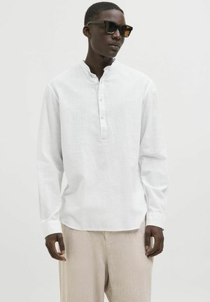 White long-sleeve shirt with a band collar, front button placket, and relaxed fit, worn with light beige textured pants and sunglasses.