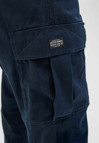 Mörkblå cargo-byxficka med klaff och synlig "Jack & Jones"-märke sydd på klaffen.