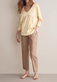 Blouse jaune clair à col en V avec des manches trois-quarts, associée à un pantalon beige à jambes droites et des sandales blanches à brides. Tissu doux.