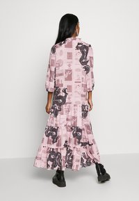 Maxi šaty z růžové látky s černým motivem draka a novinovým potiskem, s balónovými rukávy a vrstevnatými volány na spodním lemu.
