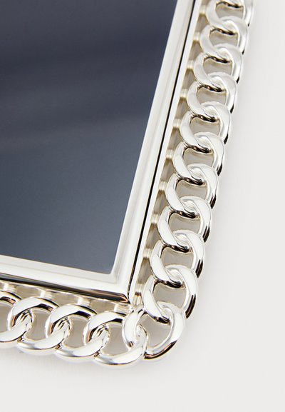 Veidrodžio rėmas sidabro spalvos, apjuostas stambaus grandinės segmentų kraštais. Rėmas blizgios apdailos, o atspindinti veidrodžio dalis yra tamsi.