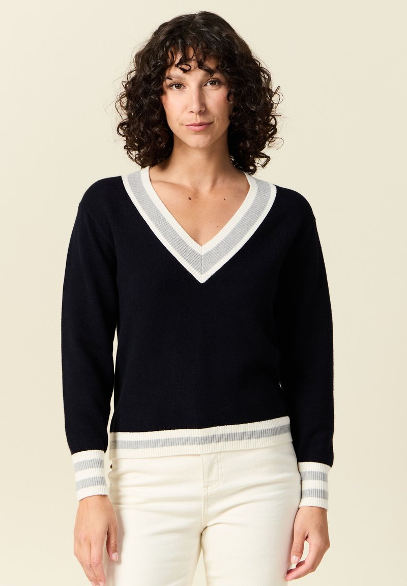 Pull à col en V bleu marine avec des rayures gris clair et blanches à l'encolure et aux poignets. Texture douce, design ajusté, manches longues et ourlet côtelé.