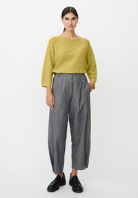 Cytrynowo żółty sweter z dzianiny z rękawami za łokieć, w połączeniu z szarą, szeroką nogawką w paski i czarnymi butami wsuwanymi.
