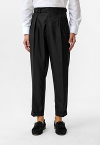 Zwarte geplooide broek met een getailleerde pasvorm, voorzien van zijzakken, een tailleband met knopen, omslagen en een gladde stoftextuur.