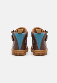 Hnědé kožené boty pro batolata s modrými patními panely, béžovými poutky, bočními zipy a texturovanými gumovými podrážkami, zobrazené zezadu.