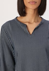 Navy and white striped blouse with a mandarin collar, featuring a v-neckline and lightweight, smooth fabric. Horizontal stripes are prominent.