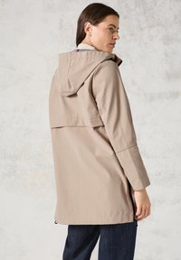Veste imperméable beige avec capuche, dotée d'un col haut, de poches latérales et d'une coupe décontractée. Le tissu semble lisse avec un léger éclat.