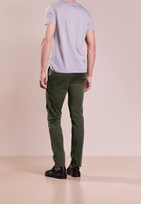 Grå kortärmad skjorta i avslappnad passform, parat med gröna byxor. Modellen har på sig svarta sneakers, med släta texturer synliga.