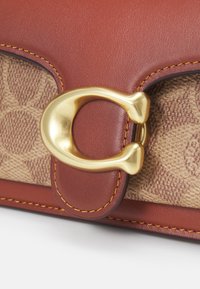 Sac en cuir marron et tissu à motifs avec une boucle métallique dorée en forme de lettre C et des coutures orange détaillées.