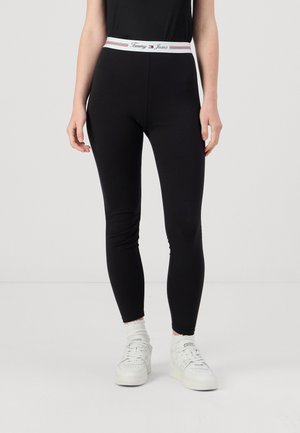 Mustat legginsit, jotka on valmistettu joustavasta kankaasta, valkoisella vyötärönauhalla, jossa on "Tommy Jeans" -teksti ja punaisia yksityiskohtia. Tiukka malli, nilkkapituiset.