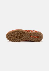 Orange athletic shoe sole with a textured rubber surface. Features circular grip patterns and a prominent "GEOX" logo in black.