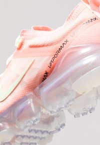 Zapatillas Nike Vapormax en suave tejido rosa con una suela translúcida. Presentan un acento verde y la marca "VAPORMAX" en negro.