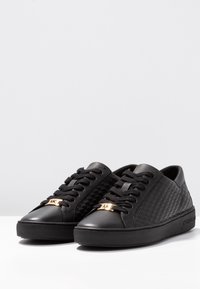 Sneakers in pelle nera con lati testurizzati, punta tonda e lacci tono su tono. Presentano un dettaglio in metallo dorato sulla linguetta e una suola nera.
