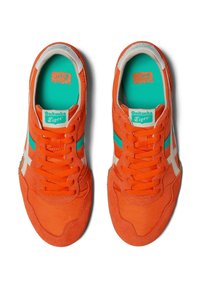Sneaker in suede arancione con accenti turchesi, caratterizzati da strisce bianche e lacci, e una linguetta imbottita, progettati per offrire comfort e stile.
