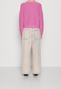 Różowy sweter na drutach z prążkowanym dołem, zestawiony z jasnymi, wyblakłymi jeansami o szerokich nogawkach, z tylnymi kieszeniami i lekko postarzanym wyglądem.