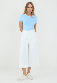 Top azzurro chiaro a maniche corte con dettaglio a chiave laterale, abbinato a pantaloni bianchi a vita alta e scarpe da ginnastica color crema.
