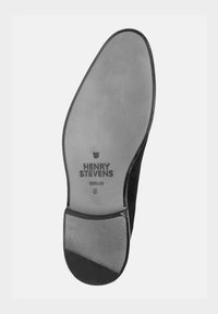 Zwarte suède schoenzool met een gestructureerde grijze inlegzool, met reliëfbranding "HENRY STEVENS BERLIN," en metalen studs langs de rand. Maat 8.