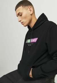 Zwarte hoodie met een voorzak, voorzien van een kleurrijk logo ontwerp. Het materiaal lijkt zacht, met een gladde textuur en verstelbare trekkoorden.
