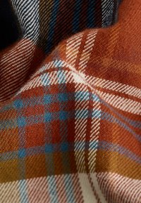 Kariertes Gewebe in verschiedenen Schattierungen von Orange, Blau, Creme und Braun, mit weicher Textur und einem gewebten Muster aus Karos.