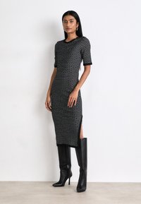 Black and white patterned dress with short sleeves, mid-calf length, side slits, and a round neckline, paired with tall black boots.