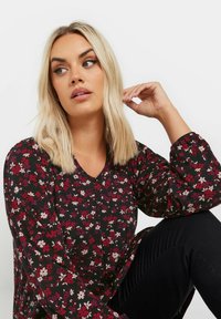 Svart blommig blus med röda och rosa mönster, v-ringning och puffiga ärmar. Buren med mörka byxor, som har subtil ribbad textur.