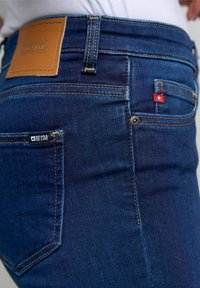 Jeans de mezclilla azul oscuro con un parche de cuero etiquetado "BIG STAR" en la cinturilla, un pequeño acento de estrella roja en el bolsillo trasero y costuras doradas.