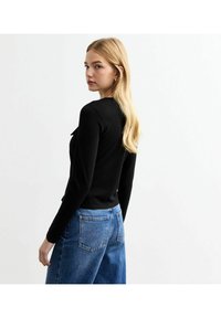 T-shirt noir à manches longues avec une silhouette ajustée, associé à un jean large taille haute bleu. Design simple, sans motifs ni accents visibles.