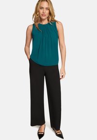 Blouse sans manches couleur sarcelle avec plis, associée à un pantalon noir taille haute à jambes larges et à des talons noirs pointus. Texture de tissu lisse.