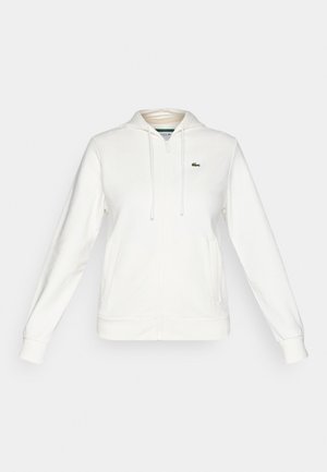 White zip-up hoodie with front pockets, drawstring hood, and a small green crocodile logo on the left chest.