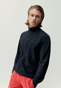 Svart zip-up jacka i lätt tyg med hög krage, med en diskret logotyp i vitt på bröstet.
