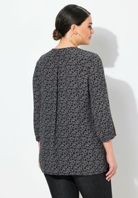 Blouse à motif floral en gris foncé, en tissu léger, manches trois-quarts, détail de pli dans le dos, légère brillance, associée à un jean sombre.