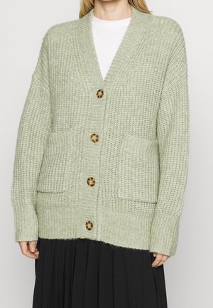 Light green cardigan made of textured knit fabric. It features a V-neck, large buttons, and front pockets. Long sleeves with ribbed cuffs.