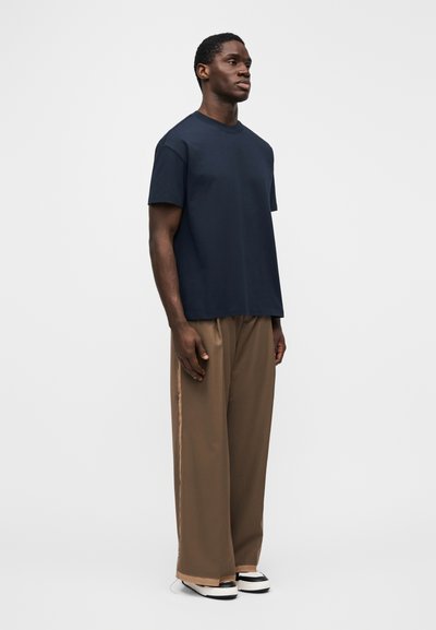 Tmavě modré bavlněné tričko s volným střihem, kulatým výstřihem a krátkými rukávy, kombinované s volnými hnědými kalhotami s kontrastním bočním pruhem.